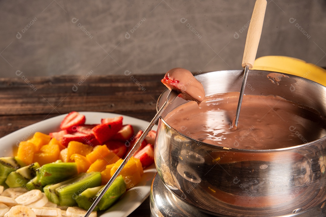 Fondue de chocolate acompanhado de frutas tropicais na mesa de madeira e fundo escuro