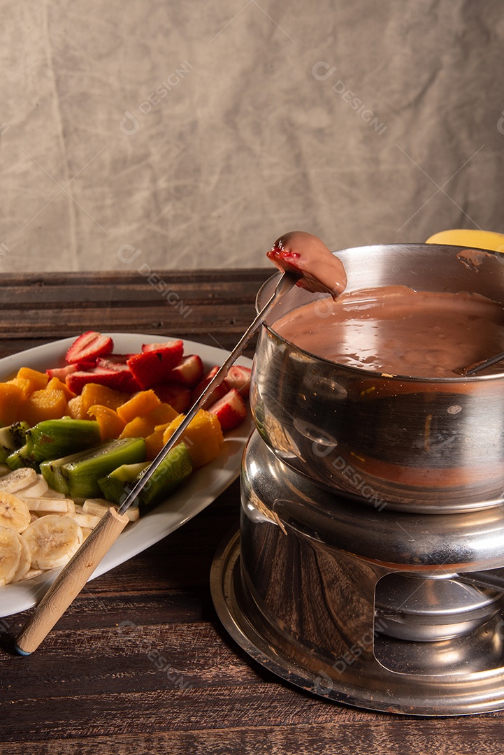 Fondue de chocolate acompanhado de frutas tropicais na mesa de madeira e fundo escuro