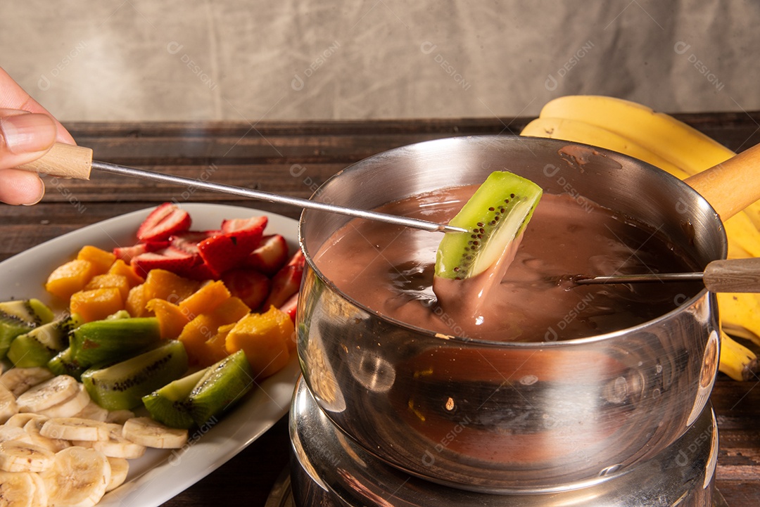 Fondue de chocolate acompanhado de frutas tropicais na mesa de madeira e fundo escuro