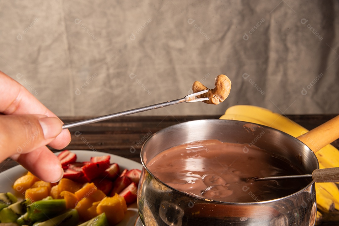 Fondue de chocolate acompanhado de frutas tropicais na mesa de madeira e fundo escuro
