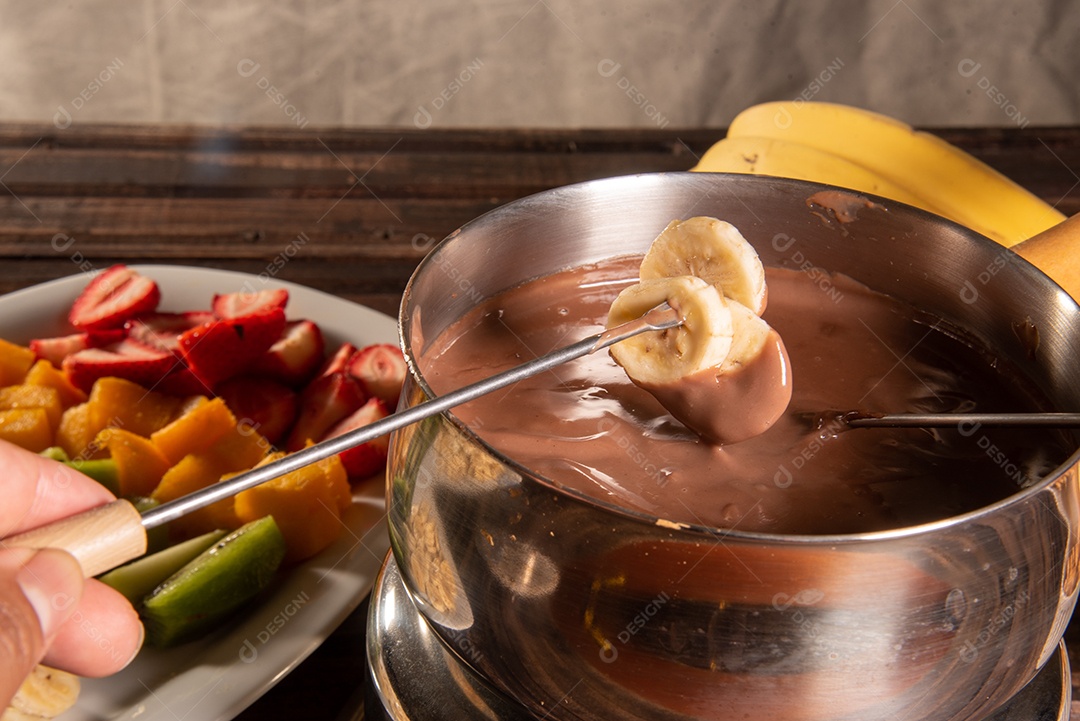 Fondue de chocolate acompanhado de frutas tropicais na mesa de madeira e fundo escuro