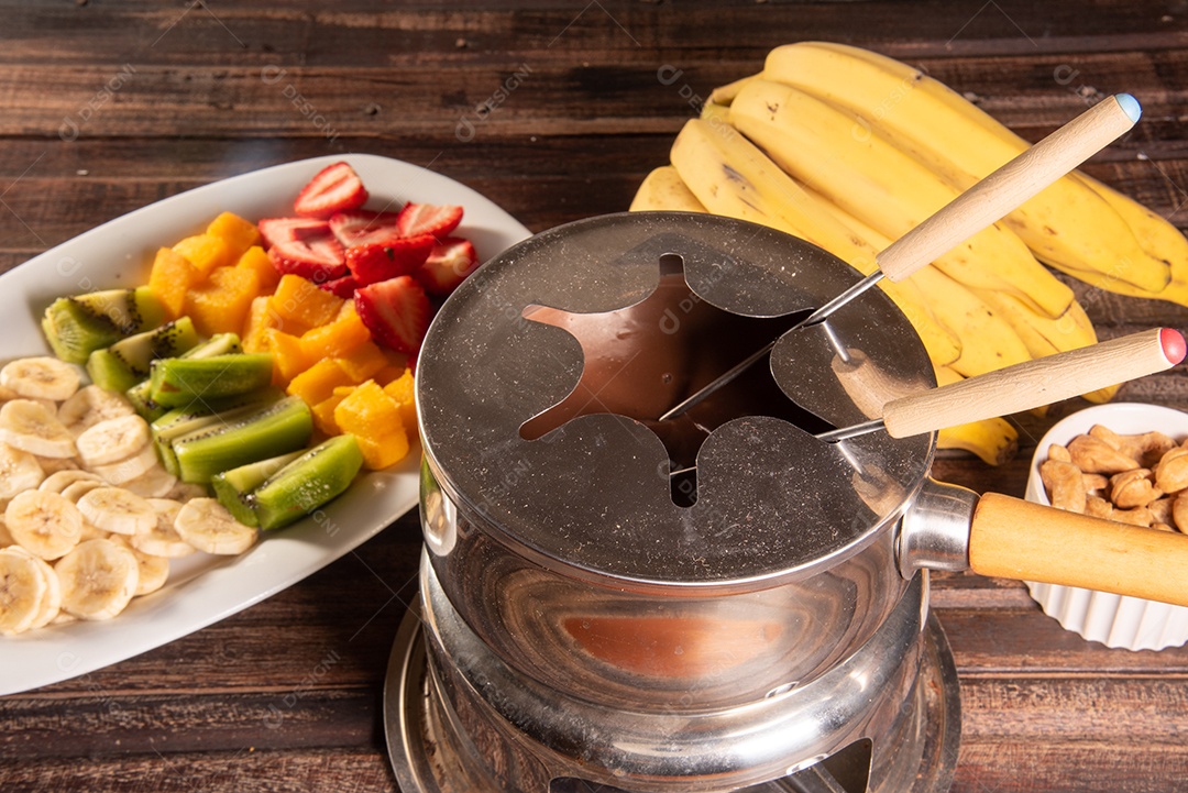 Fondue de chocolate acompanhado de frutas tropicais na mesa de madeira e fundo escuro