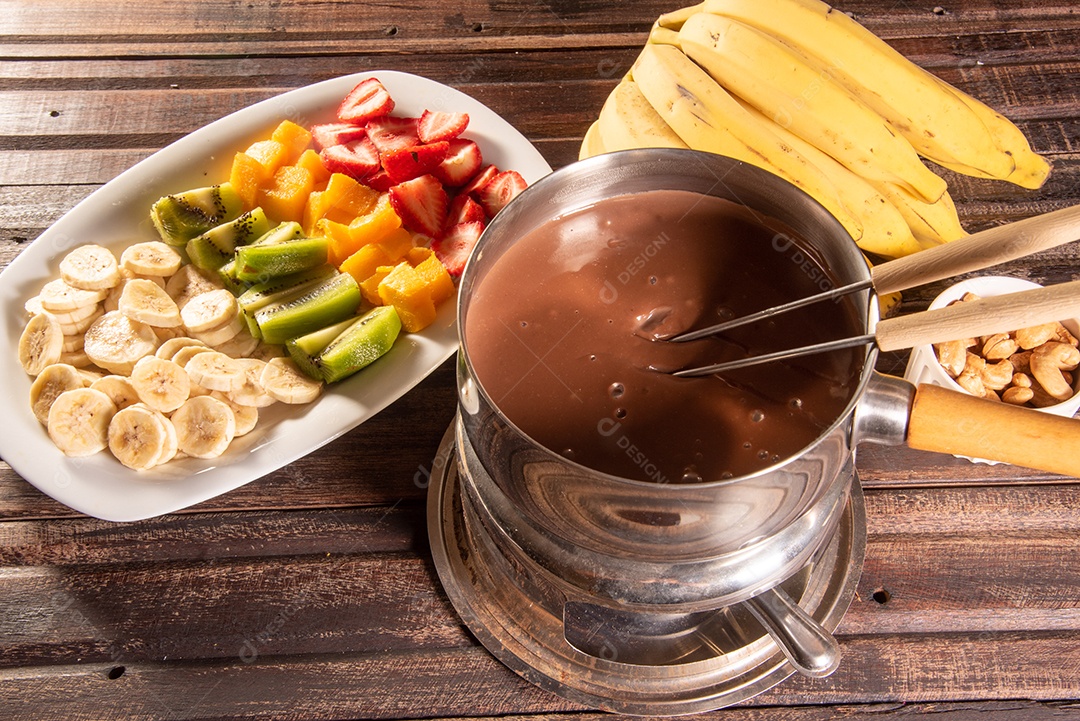 Fondue de chocolate acompanhado de frutas tropicais na mesa de madeira e fundo escuro