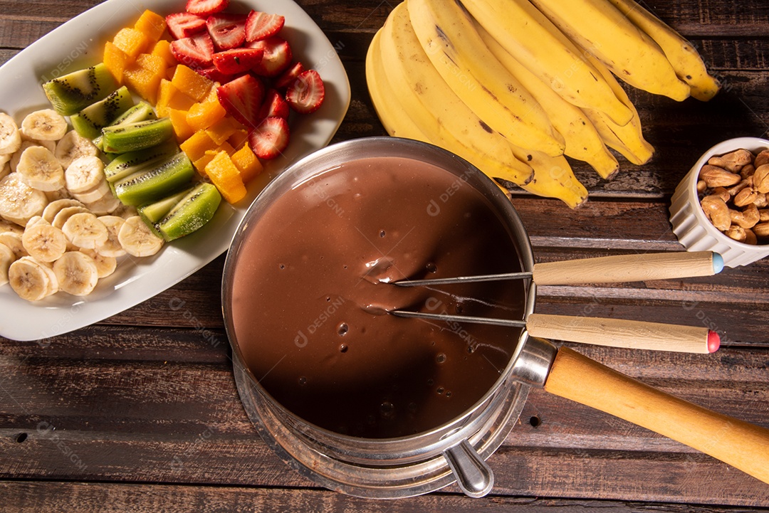Fondue de chocolate acompanhado de frutas tropicais na mesa de madeira e fundo escuro