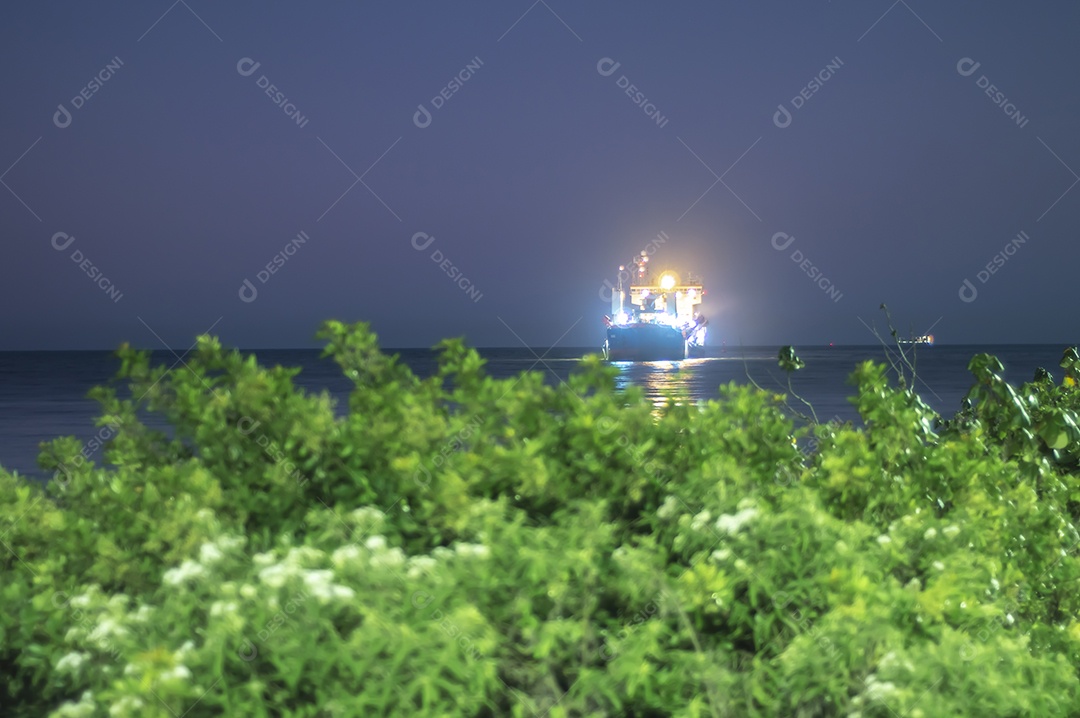 Navio de carga navegando no mar à noite com luzes acesas, foto em longa exposição.