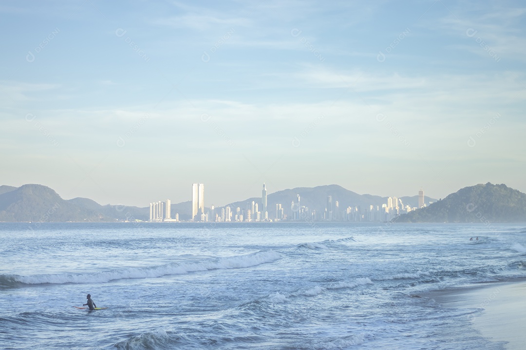 Praia brava em itajai-sc brasil com a cidade de balneário comboriu ao fundo e gente curtindo a praia conhecida por suas ondas altas.