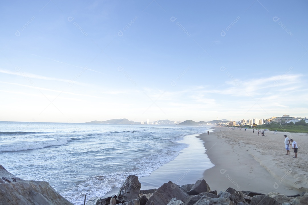 Praia brava em itajai-sc brasil com a cidade de balneário comboriu ao fundo e gente curtindo a praia conhecida por suas ondas altas.