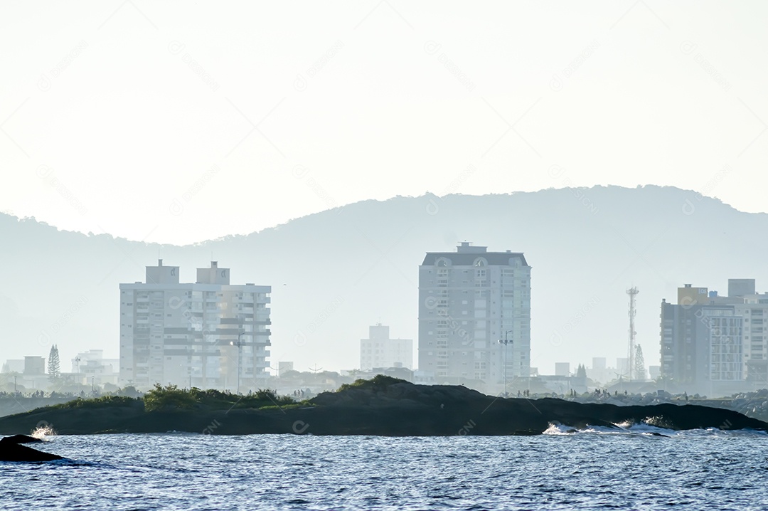 Crianças a brincar numa ilha à beira-mar, fim de tarde com montanhas ao fundo e mar à frente