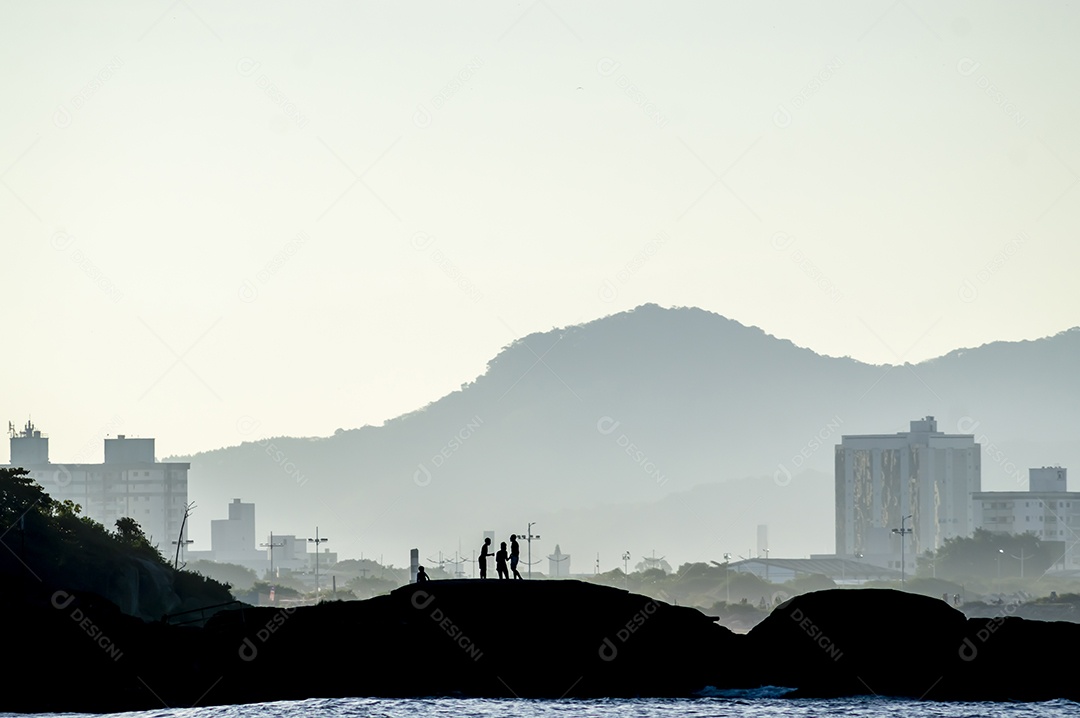 Crianças a brincar numa ilha à beira-mar, fim de tarde com montanhas ao fundo e mar à frente