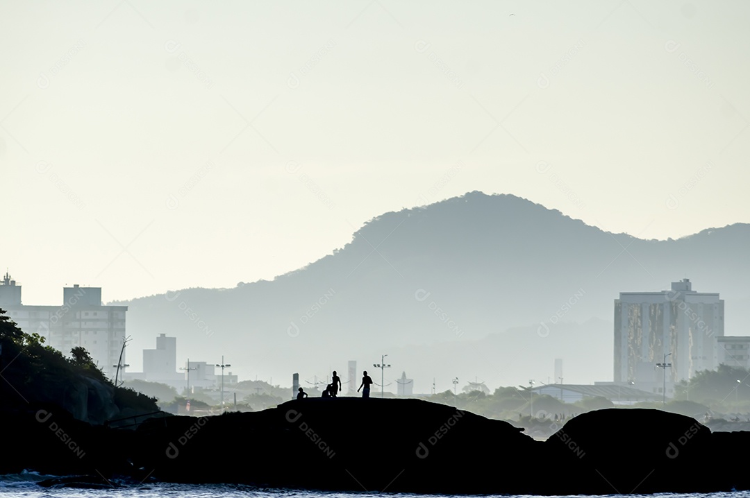 Crianças a brincar numa ilha à beira-mar, fim de tarde com montanhas ao fundo e mar à frente
