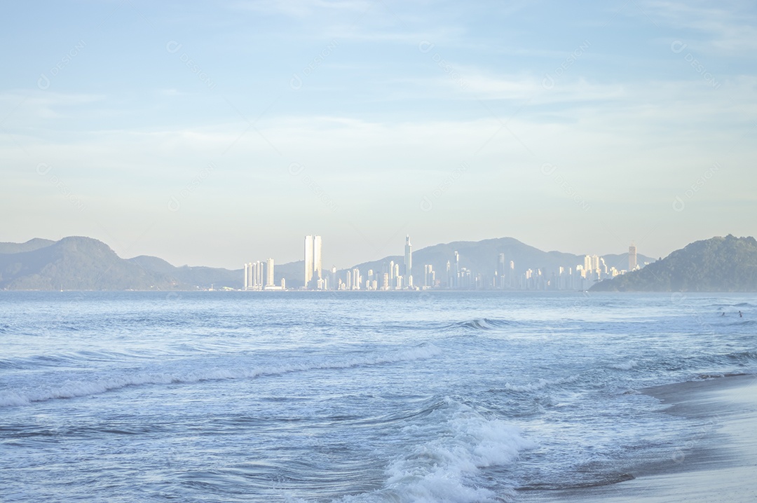 Praia brava em itajai-sc brasil com a cidade de balneário comboriu ao fundo e gente curtindo a praia conhecida por suas ondas altas.