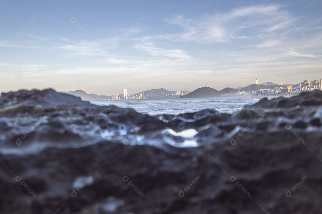 Pedras molhadas pelas ondas do mar e cidade de balneário camboriu-sc brasil ao fundo, conceito de praia e turismo.