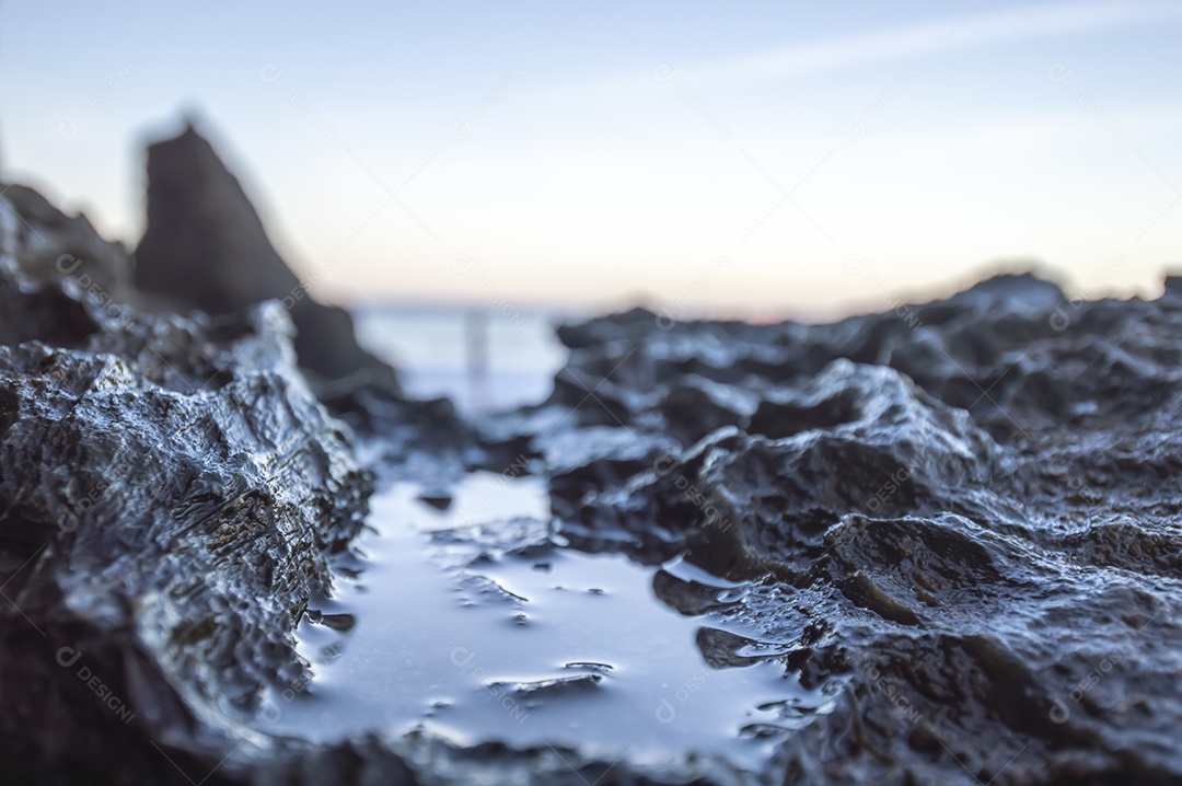 Pedras molhadas pelas ondas do mar e bandeira vermelha no oceano ao fundo, textura com pedras e mar, conceito de ondas do mar.