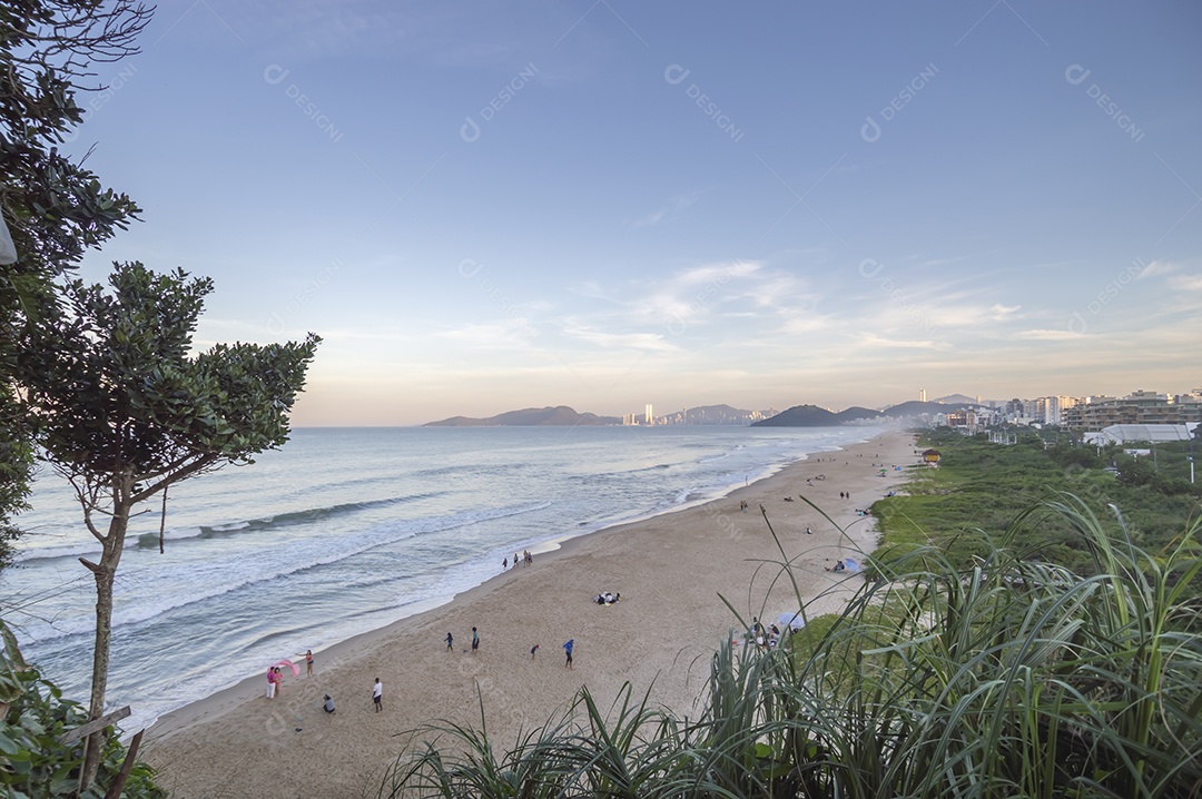 Praia brava em itajai-sc brasil com a cidade de balneário comboriu ao fundo e gente curtindo a praia conhecida por suas ondas altas.