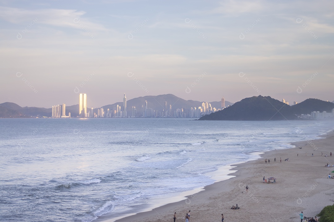 Praia brava em itajai-sc brasil com a cidade de balneário comboriu ao fundo e gente curtindo a praia conhecida por suas ondas altas.