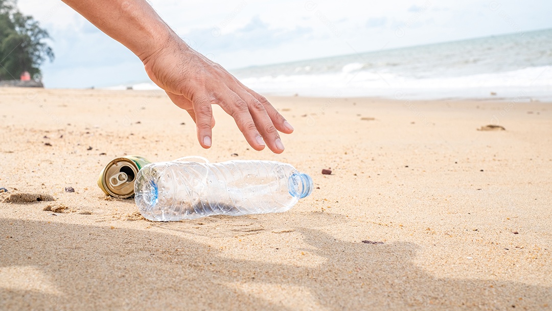 Mão pegando limpeza de garrafas plásticas na praia.