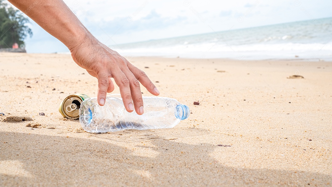 Mão pegando limpeza de garrafas plásticas na praia.