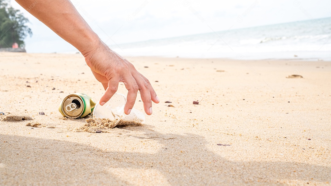 Mão pegando limpeza de garrafas plásticas na praia.