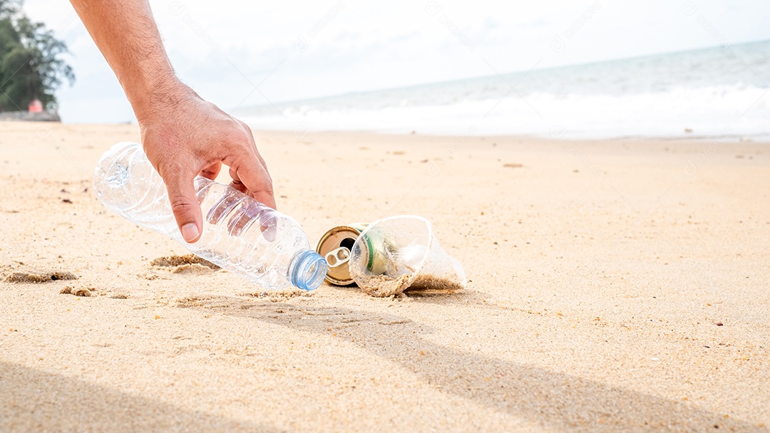 Mão pegando limpeza de garrafas plásticas na praia.