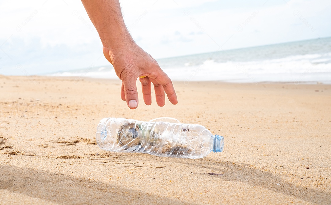 Mão pegando limpeza de garrafas plásticas na praia.