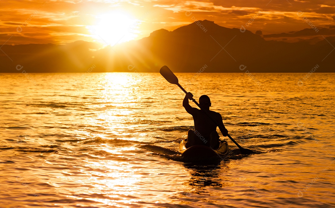 Silhueta de homem ao pôr do sol remando em seu caiaque na costa do Brasil