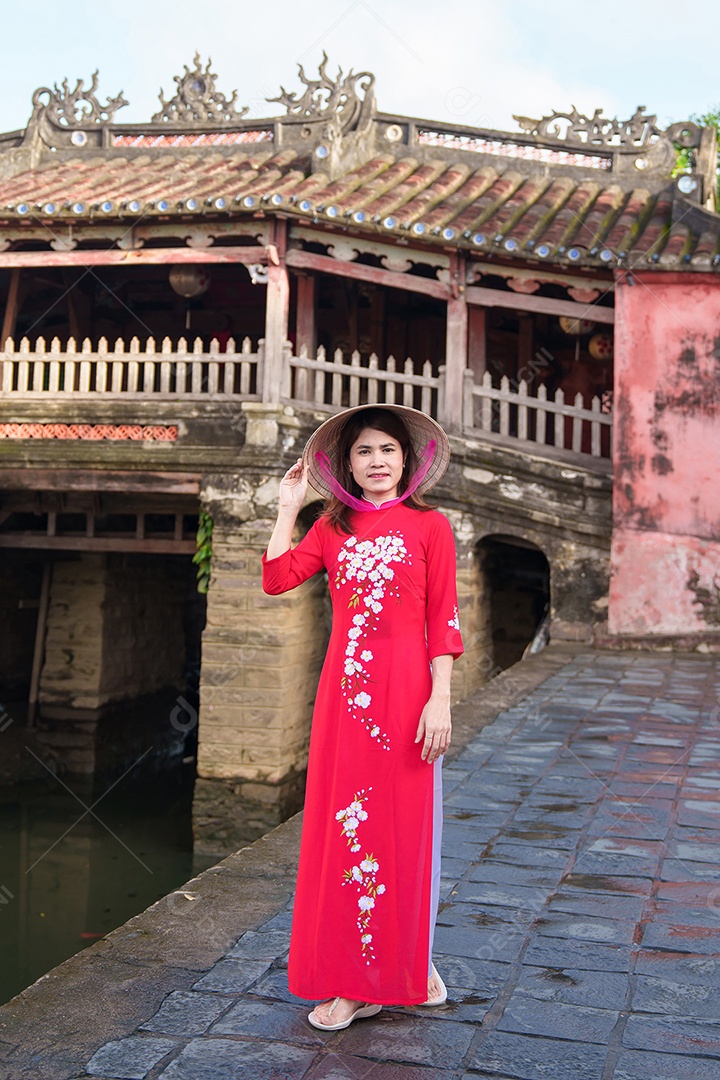 Mulher viajante usando vestido vietnamita Ao Dai passeando na ponte coberta japonesa na cidade de Hoi An, Vietnã.
