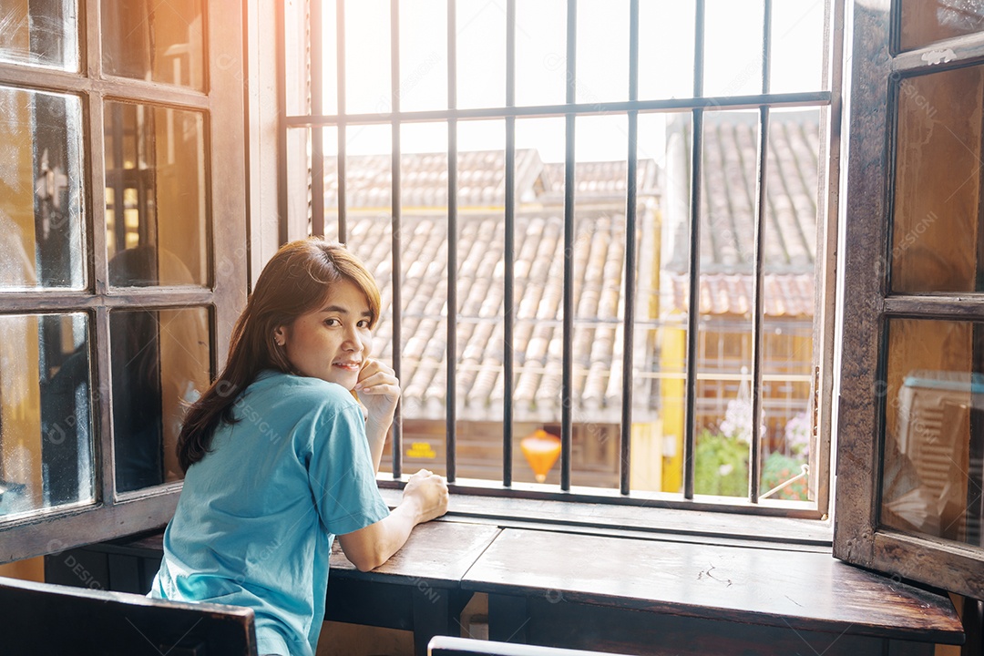 Mulher feliz sentada perto da janela sob o sol da manhã