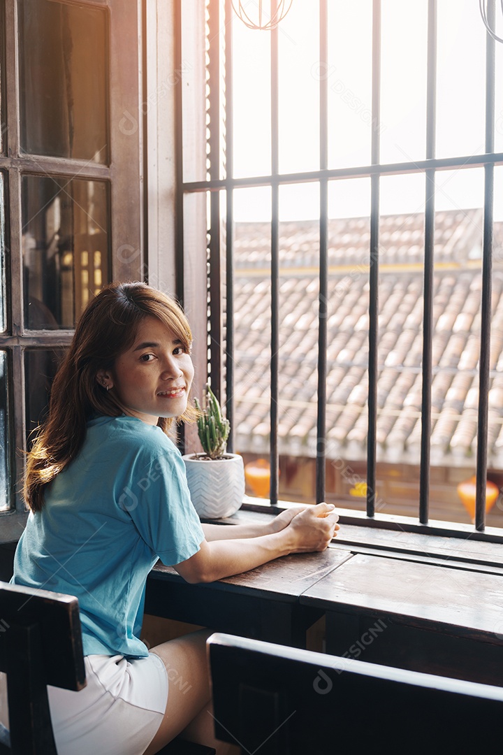 Mulher feliz sentada perto da janela sob o sol da manhã