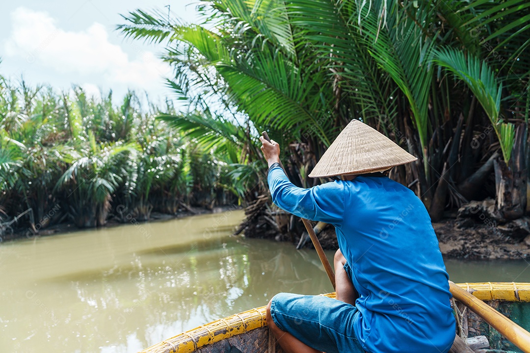 Homem remando um barco de cesta, ao longo da floresta do rio de coco