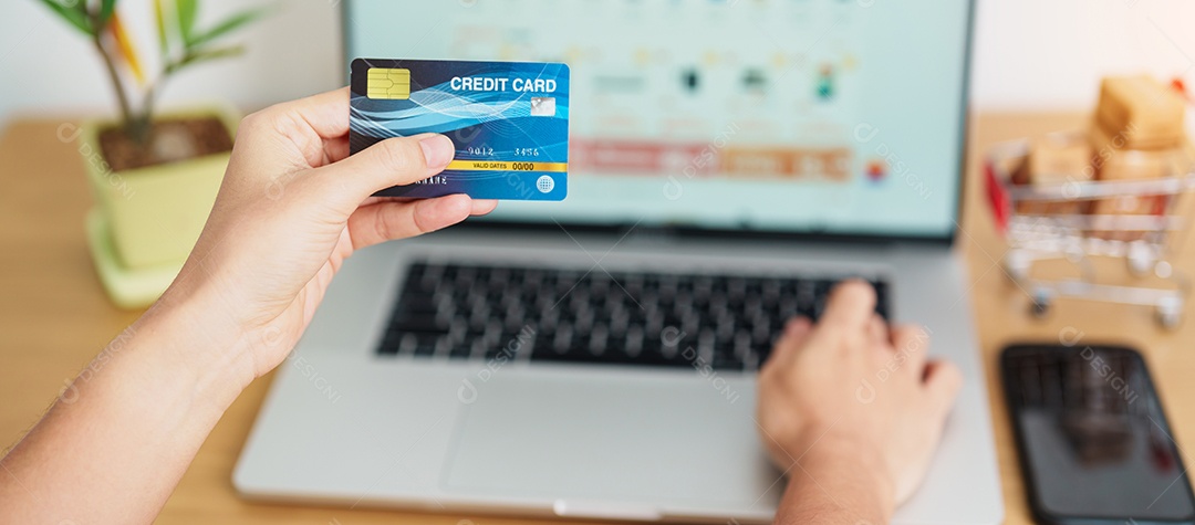 mão de uma mulher segurando o cartão de crédito e usando o laptop com o celular para fazer compras on-line enquanto faz o pedido.