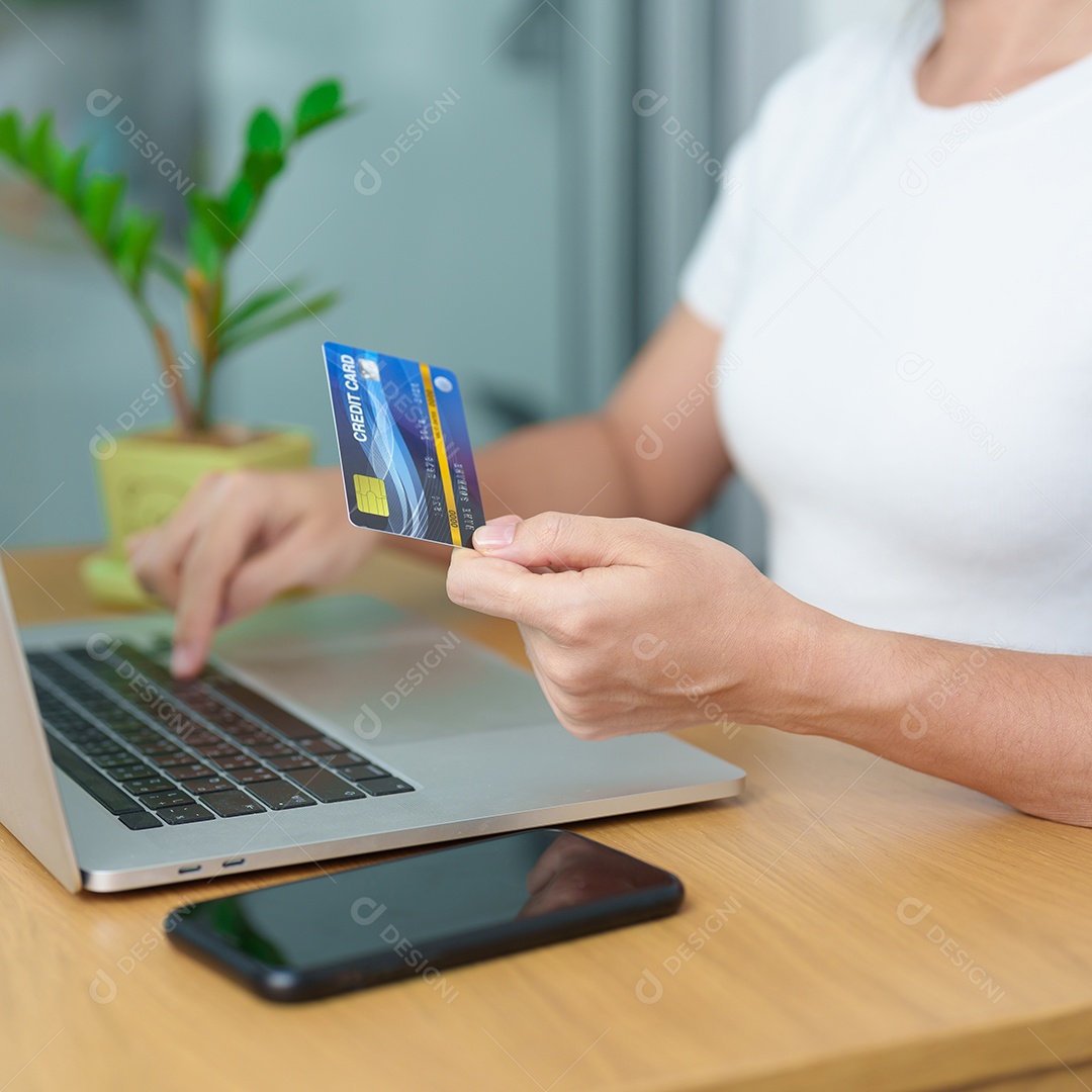 mão de uma mulher segurando o cartão de crédito e usando o laptop com o celular para fazer compras on-line enquanto faz o pedido.