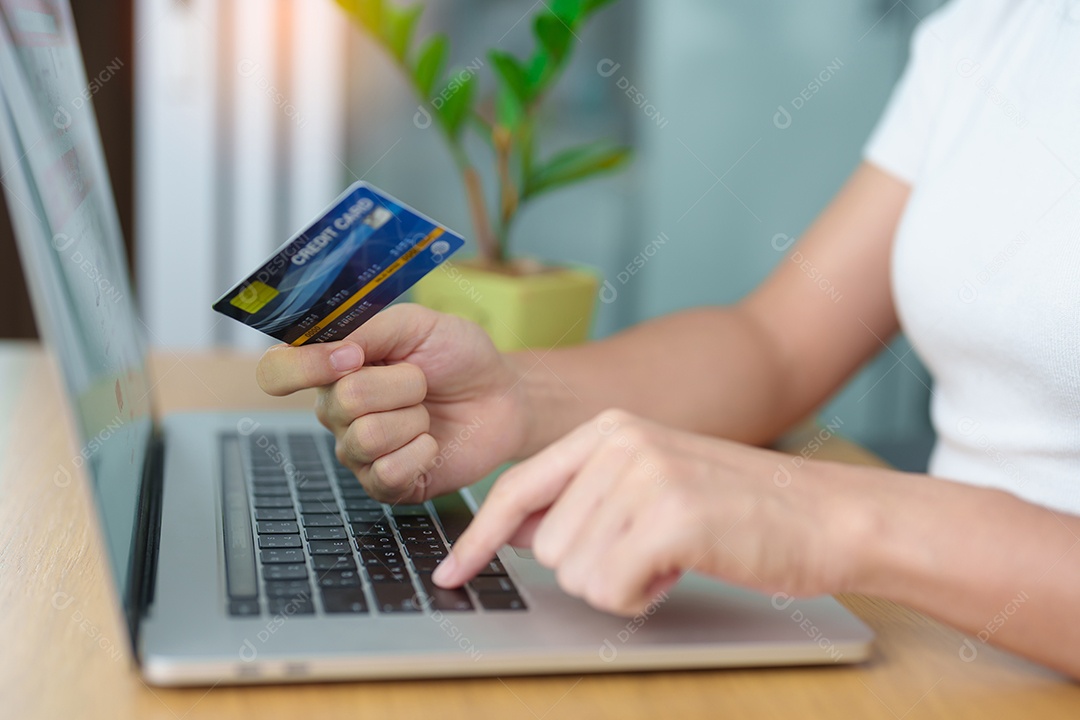 mão de uma mulher segurando o cartão de crédito e usando o laptop com o celular para fazer compras on-line enquanto faz o pedido.