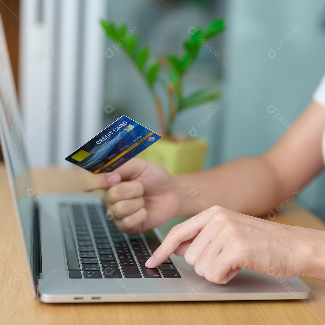 mão de uma mulher segurando o cartão de crédito e usando o laptop com o celular para fazer compras on-line enquanto faz o pedido.