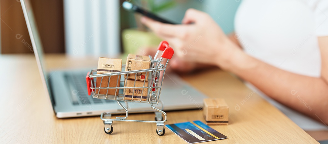 mão de uma mulher segurando o cartão de crédito e usando o laptop com o celular para fazer compras on-line enquanto faz o pedido.