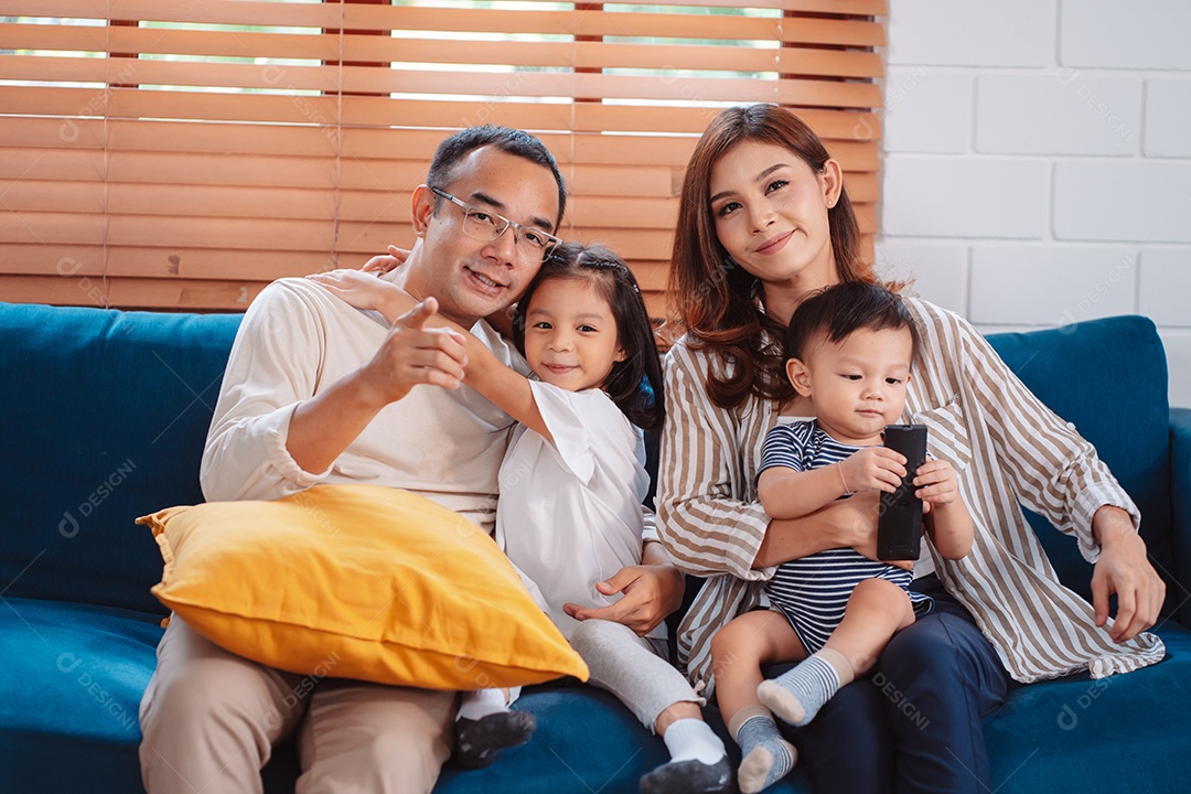 Família asiática composta por pais, filho feliz e filha assistindo TV ou filme juntos no sofá na sala de estar em casa.