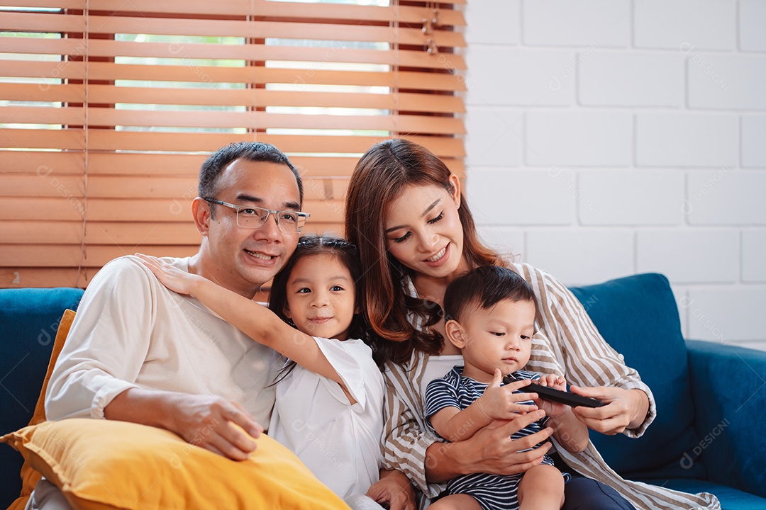 Família asiática composta por pais, filho feliz e filha assistindo TV ou filme juntos no sofá na sala de estar em casa.