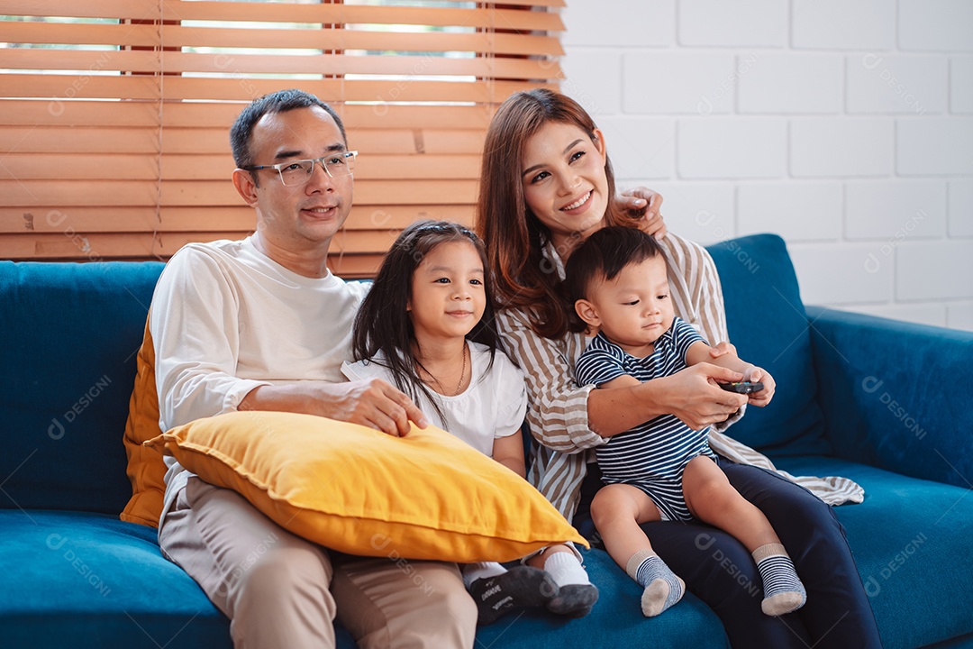 Família asiática composta por pais, filho feliz e filha assistindo TV ou filme juntos no sofá na sala de estar em casa.
