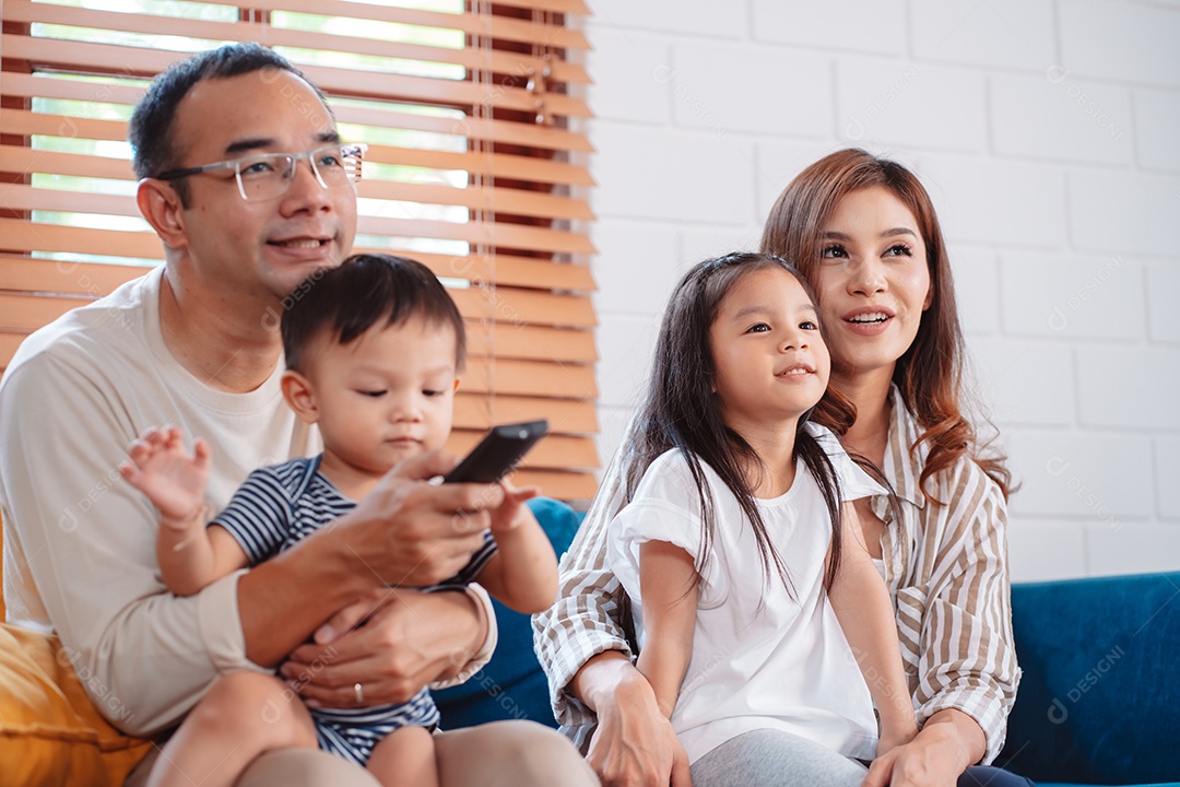 Família asiática composta por pais, filho feliz e filha assistindo TV ou filme juntos no sofá na sala de estar em casa.