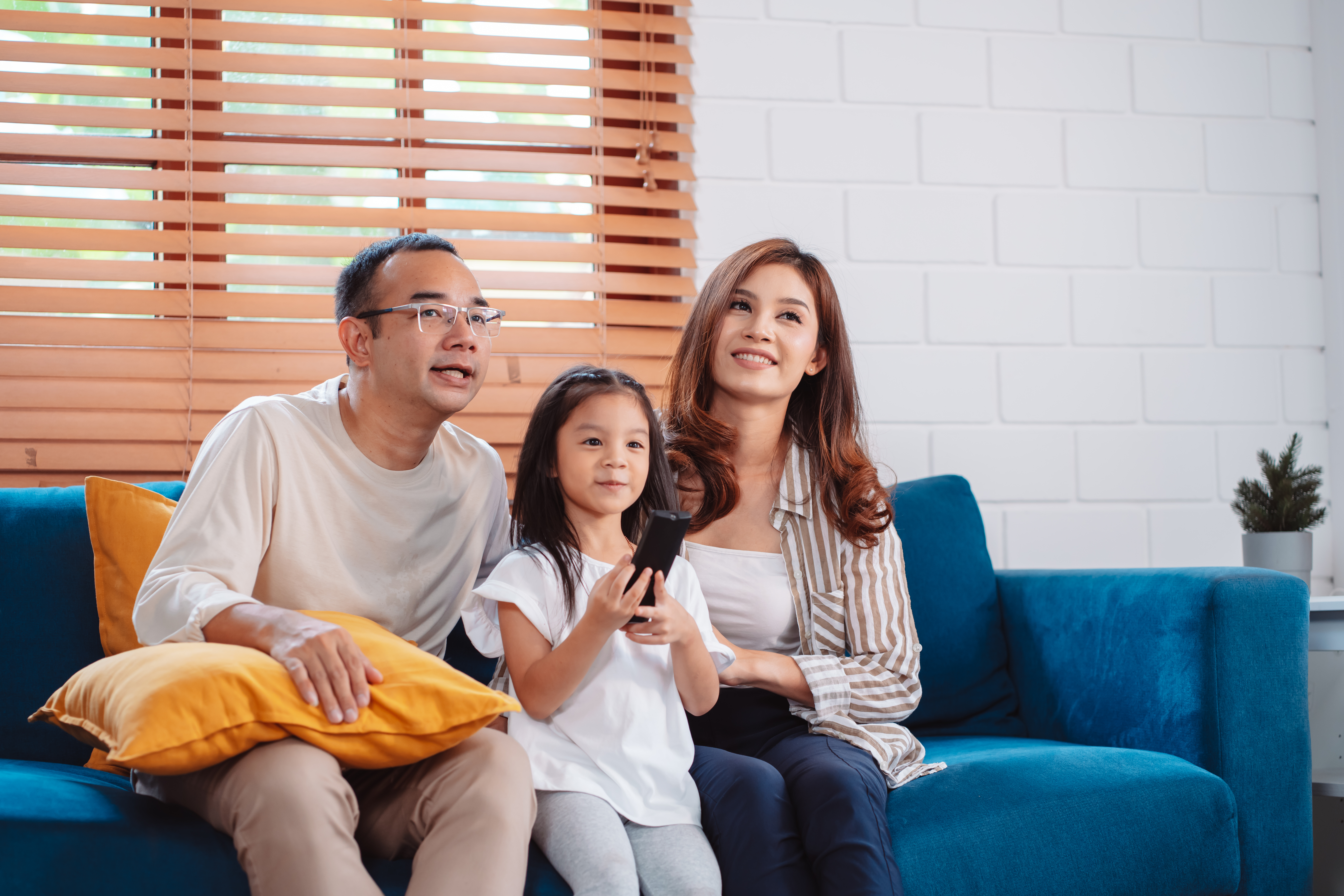 Família asiática composta por pais, filho feliz e filha assistindo TV ou filme juntos no sofá na sala de estar em casa.