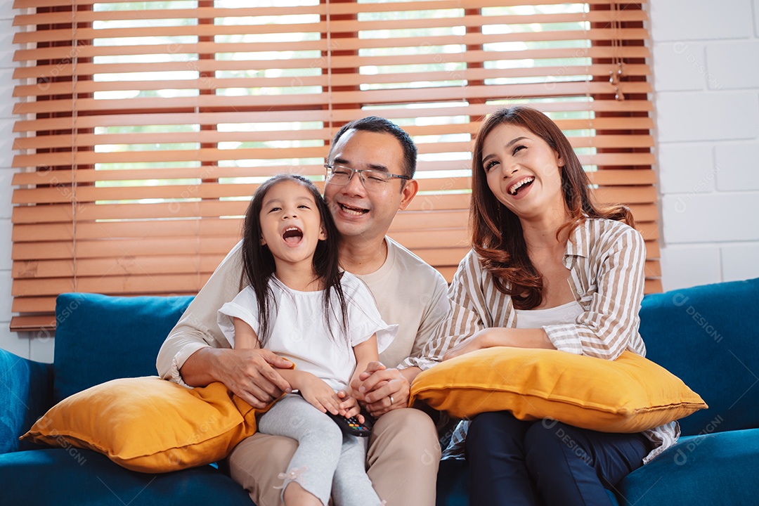 Família asiática composta por pais felizes e filha assistindo TV ou filme juntos no sofá na sala de estar em casa.