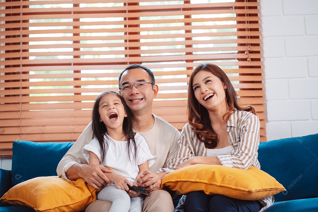 Família asiática composta por pais, filho feliz e filha assistindo TV ou filme juntos no sofá na sala de estar em casa.