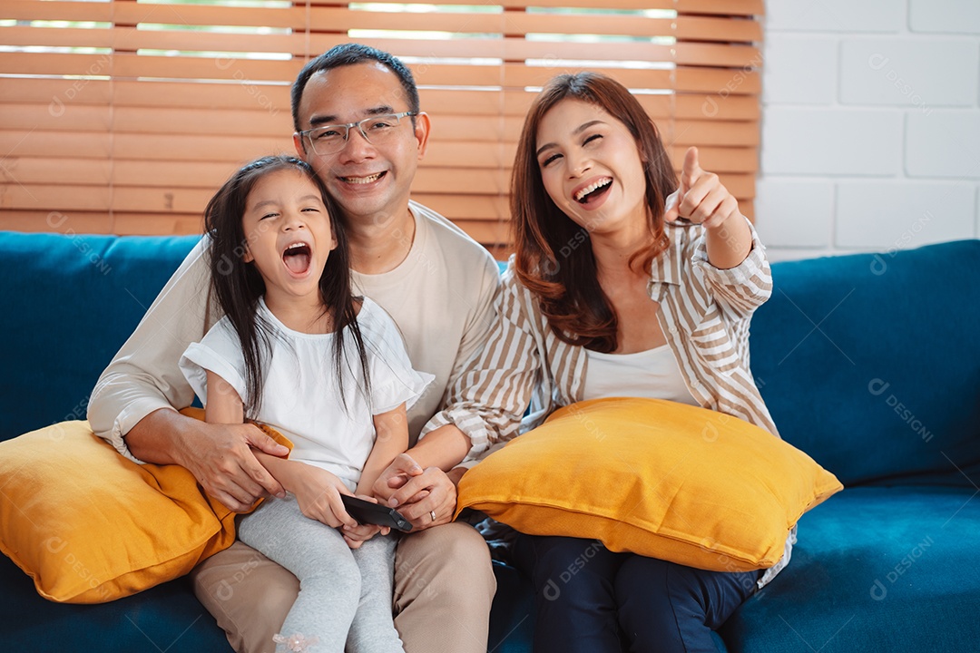 Família asiática composta por pais, filho feliz e filha assistindo TV ou filme juntos no sofá na sala de estar em casa.