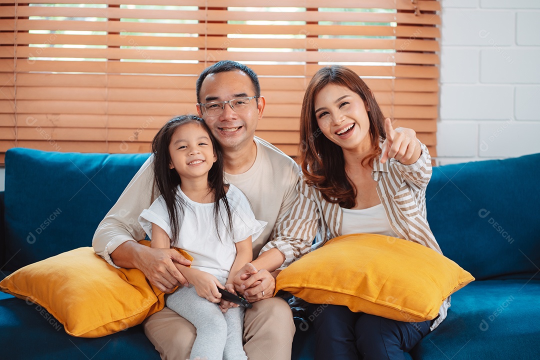 Família asiática composta por pais, filho feliz e filha assistindo TV ou filme juntos no sofá na sala de estar em casa.