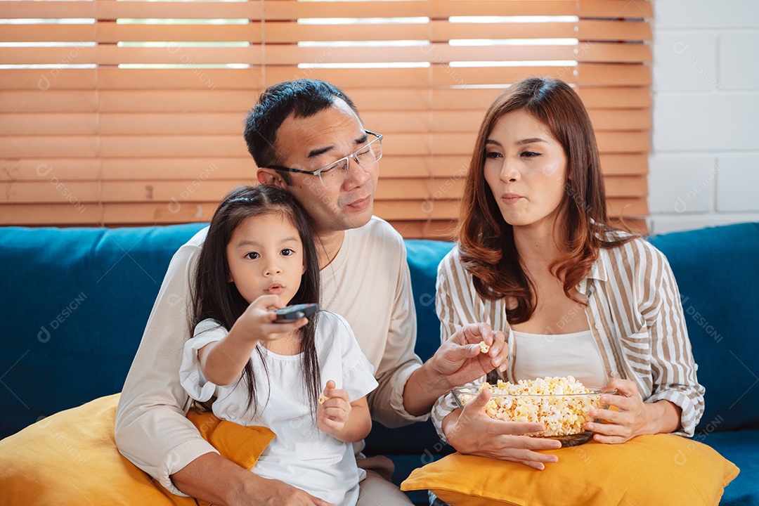 Família asiática composta por pais, filho feliz e filha assistindo TV ou filme juntos no sofá na sala de estar em casa.