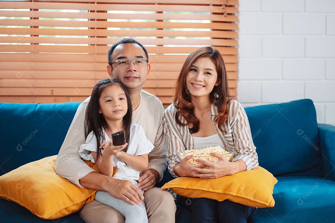 Família asiática composta por pais, filho feliz e filha assistindo TV ou filme juntos no sofá na sala de estar em casa.