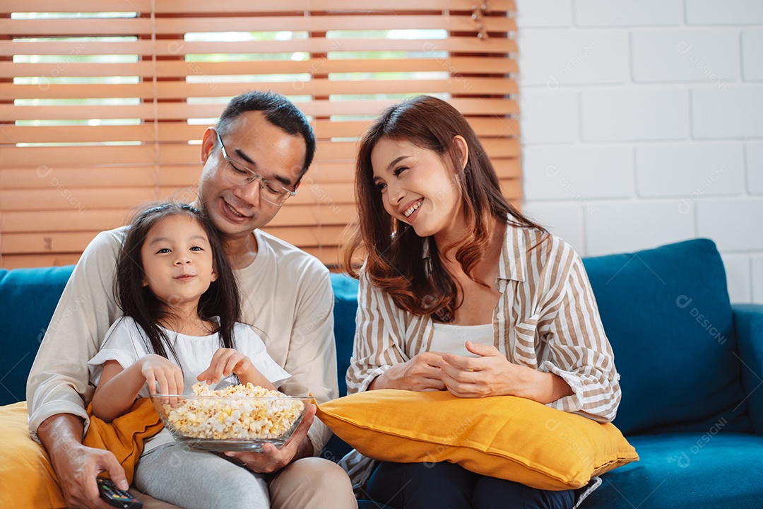 Família asiática composta por pais, filho feliz e filha assistindo TV ou filme juntos no sofá na sala de estar em casa.