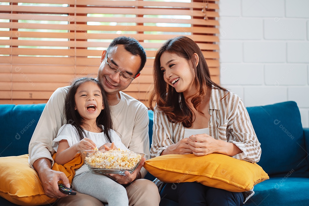 Família asiática composta por pais, filho feliz e filha assistindo TV ou filme juntos no sofá na sala de estar em casa.