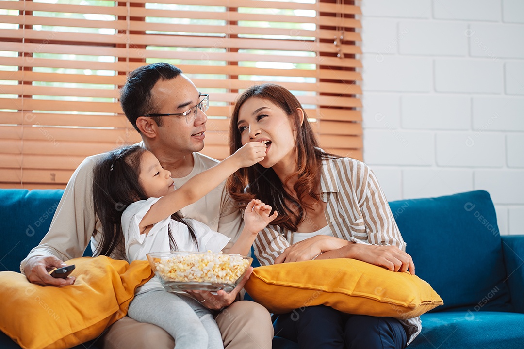 Família asiática composta por pais, filho feliz e filha assistindo TV ou filme juntos no sofá na sala de estar em casa.