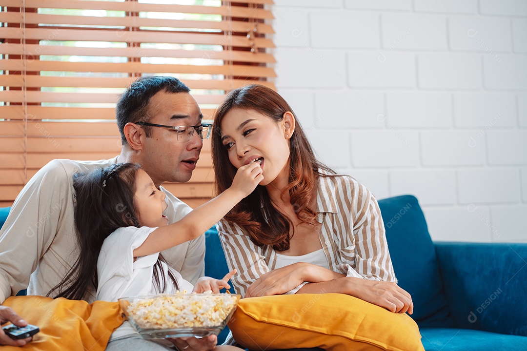 Família asiática composta por pais, filho feliz e filha assistindo TV ou filme juntos no sofá na sala de estar em casa.