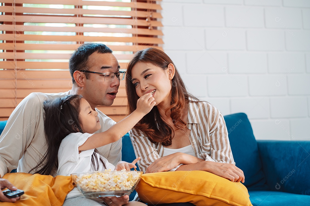 Família asiática composta por pais, filho feliz e filha assistindo TV ou filme juntos no sofá na sala de estar em casa.
